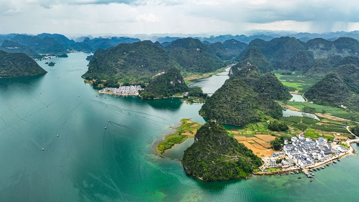 在广西壮族自治区靖西市渠洋镇东风村，波光粼粼的水面与民居、游船、群山相映成景，构成一幅生态宜居的美丽乡村画卷。