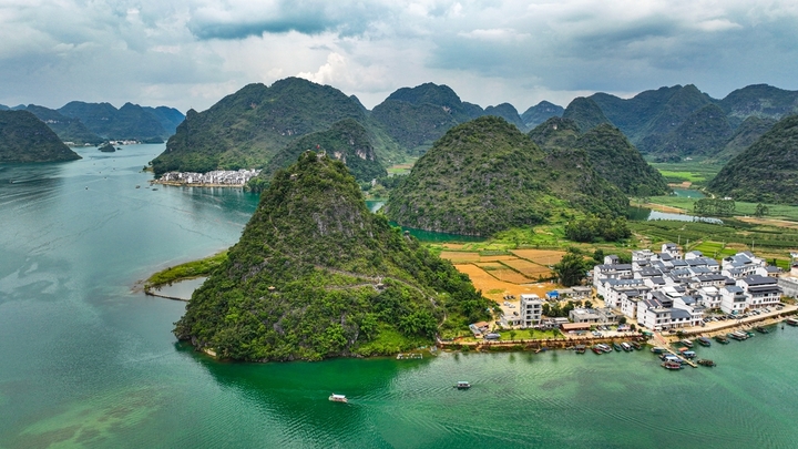 在广西壮族自治区靖西市渠洋镇东风村，波光粼粼的水面与民居、游船、群山相映成景，构成一幅生态宜居的美丽乡村画卷。