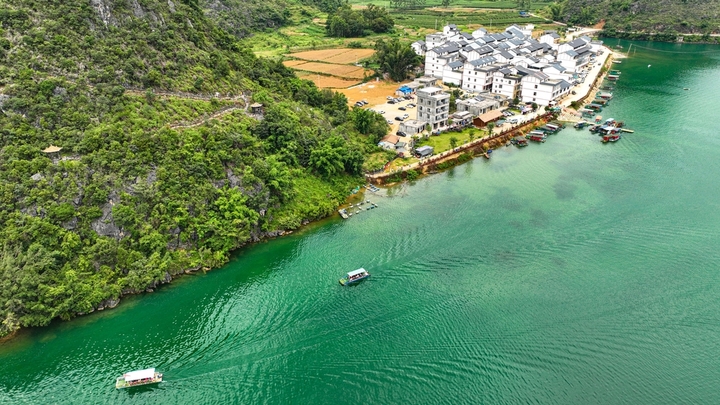 在广西壮族自治区靖西市渠洋镇东风村，波光粼粼的水面与民居、游船、群山相映成景，构成一幅生态宜居的美丽乡村画卷。