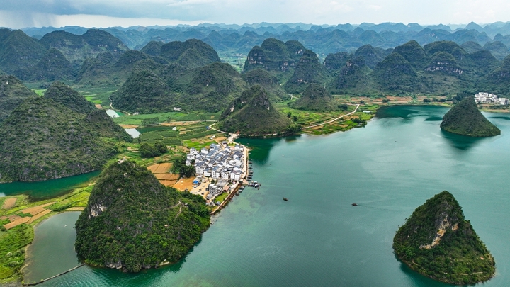 在广西壮族自治区靖西市渠洋镇东风村，波光粼粼的水面与民居、游船、群山相映成景，构成一幅生态宜居的美丽乡村画卷。IC photo