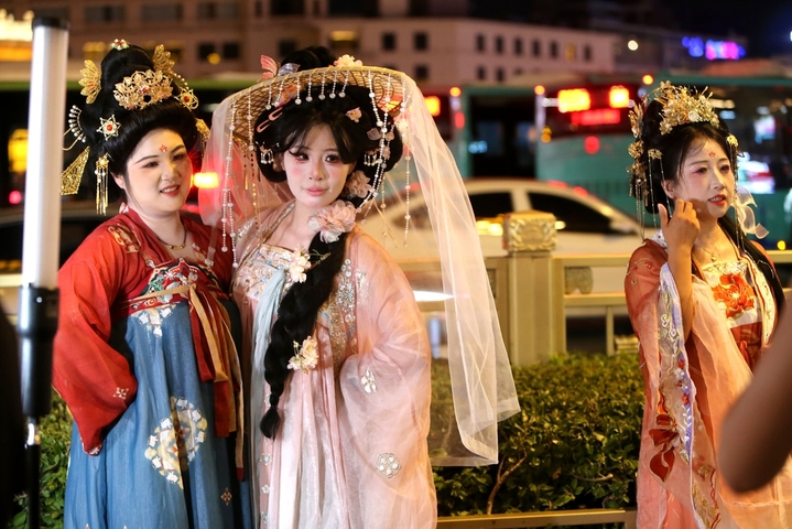 2025年8月14日晚上，陕西省西安市，无数游客身着不同风格的服饰，化着精致的妆容，带着形形色色的道具在西安钟楼下拍照，形成古城西安独特的美丽风景。