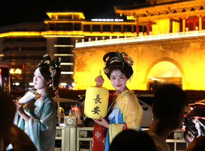 2025年8月14日晚上，陕西省西安市，无数游客身着不同风格的服饰，化着精致的妆容，带着形形色色的道具在西安钟楼下拍照，形成古城西安独特的美丽风景。