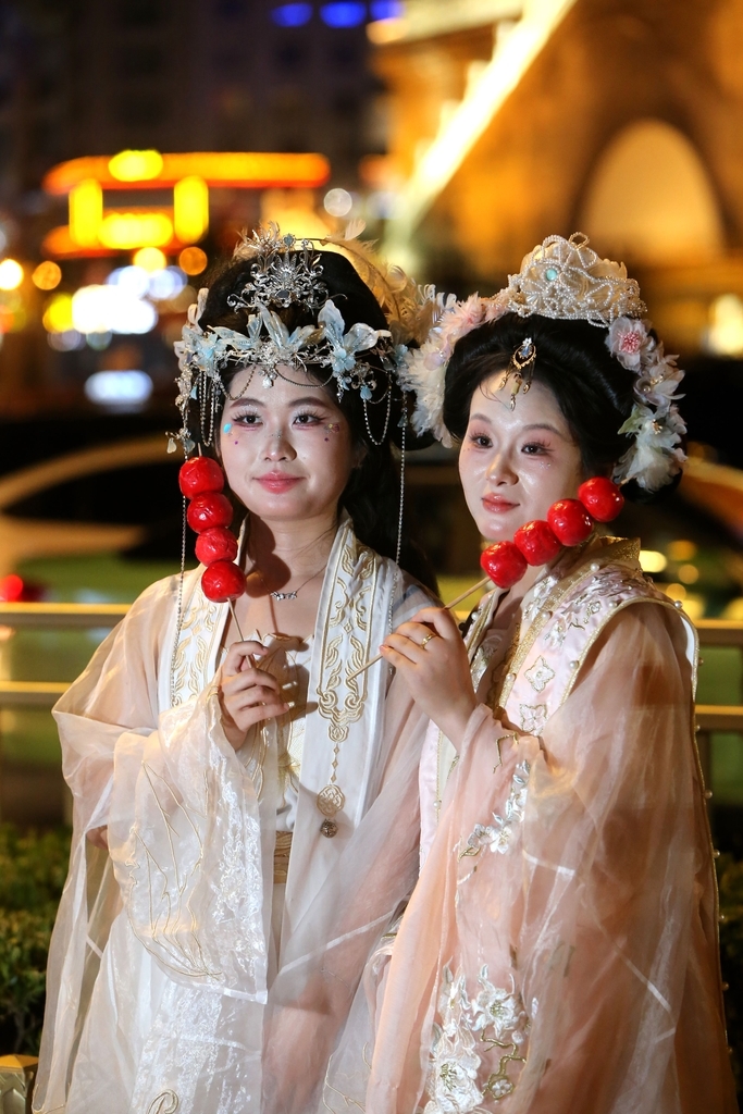 2025年8月14日晚上，陕西省西安市，无数游客身着不同风格的服饰，化着精致的妆容，带着形形色色的道具在西安钟楼下拍照，形成古城西安独特的美丽风景。