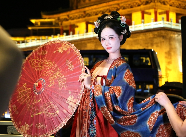 2025年8月14日晚上，陕西省西安市，无数游客身着不同风格的服饰，化着精致的妆容，带着形形色色的道具在西安钟楼下拍照，形成古城西安独特的美丽风景。