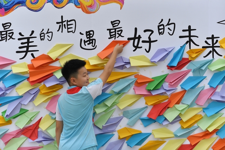 2025年8月30日，小朋友在山东省青岛市城阳区夏庄街道古镇小学开学日活动上粘贴纸飞机，寄语开学理想。

