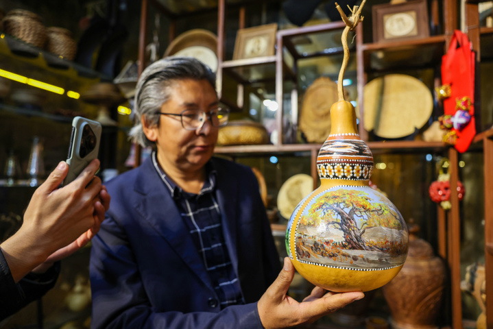 2025年9月26日晚，在新疆阿克苏市老街，非遗传承人木扎帕尔·艾斯卡尔给游客展示他创作的葫芦绘画作品。木扎帕尔出生在绘画世家，儿时便跟随爷爷、父亲学习在葫芦上绘画、雕刻，多年来，他凭借炉火纯青的技艺，让普通的葫芦焕发新生。