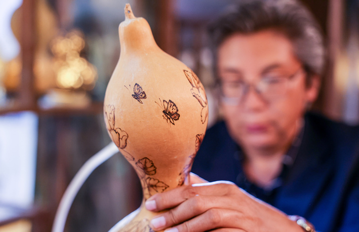 2025年9月26日晚，在新疆阿克苏市老街，非遗传承人木扎帕尔·艾斯卡尔给游客展示他创作的葫芦绘画作品。木扎帕尔出生在绘画世家，儿时便跟随爷爷、父亲学习在葫芦上绘画、雕刻，多年来，他凭借炉火纯青的技艺，让普通的葫芦焕发新生。