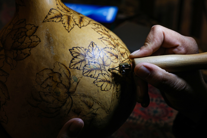 2025年9月26日晚，在新疆阿克苏市老街，非遗传承人木扎帕尔·艾斯卡尔给游客展示他创作的葫芦绘画作品。木扎帕尔出生在绘画世家，儿时便跟随爷爷、父亲学习在葫芦上绘画、雕刻，多年来，他凭借炉火纯青的技艺，让普通的葫芦焕发新生。