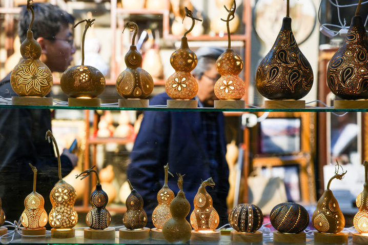 2025年9月26日晚，在新疆阿克苏市老街，非遗传承人木扎帕尔·艾斯卡尔给游客展示他创作的葫芦绘画作品。木扎帕尔出生在绘画世家，儿时便跟随爷爷、父亲学习在葫芦上绘画、雕刻，多年来，他凭借炉火纯青的技艺，让普通的葫芦焕发新生。