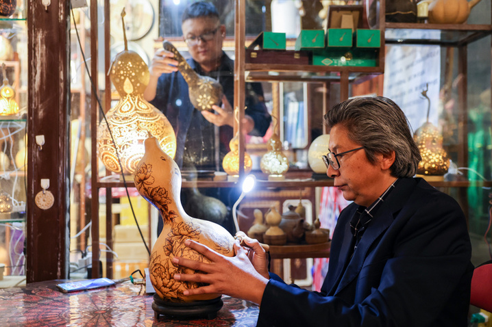 2025年9月26日晚，在新疆阿克苏市老街，非遗传承人木扎帕尔·艾斯卡尔创作葫芦烙画。木扎帕尔出生在绘画世家，儿时便跟随爷爷、父亲学习在葫芦上绘画、雕刻，多年来，他凭借炉火纯青的技艺，让普通的葫芦焕发新生。来源：张宇(摄影部)/中新社/视觉中国