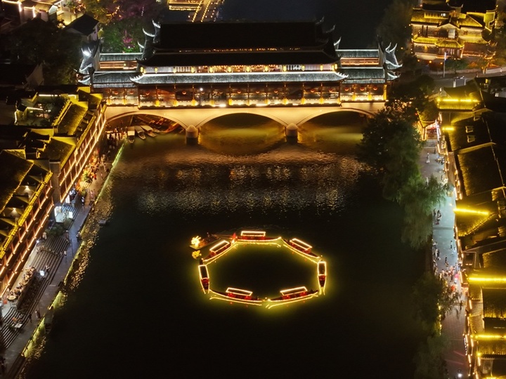 2025年10月5日晚，中秋节将至，湖南凤凰古城沱江上，百米灯光金龙游船拼接出圆月图案。金龙游船首尾相接，与两岸吊脚楼灯火相映，吸引游客沉浸式感受古城中秋氛围。