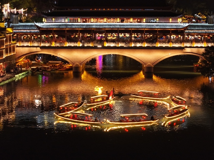 2025年10月5日晚，中秋节将至，湖南凤凰古城沱江上，百米灯光金龙游船拼接出圆月图案。金龙游船首尾相接，与两岸吊脚楼灯火相映，吸引游客沉浸式感受古城中秋氛围。