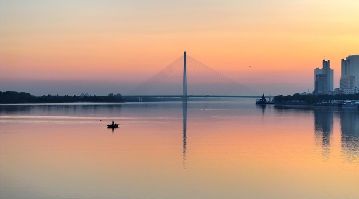 2025年10月24日，黑龙江省哈尔滨市，初冬的清晨，松花江水平如镜，倒映着天边微光。一艘艘小渔船轻划江面，渔民们娴熟地起网、下网，银丝渔网在晨光中闪烁，网上跃动的鱼影与波光交织。金黄的晨光铺满江面，将渔船、渔网和渔民的剪影染成温暖的金色，宛如一曲无声的渔光曲。江面倒影摇曳，渔船与天际线融为一体，构成一幅静谧而生动的初冬捕鱼图。