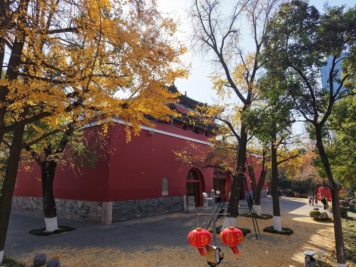 2025年12月9日，南京秋高气爽，鼓楼公园秋色斑斓，周边的树木各色交织，与古朴、砖红色的古建筑相映，如一幅画卷，美不胜收！