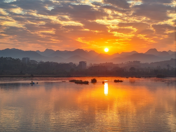 2025年12月15日，广西桂林，太阳从远处的山顶渐渐升起，温暖的阳光照耀着远处的山峦和村庄，映红了湘江，江面上的小舟在收拾渔获，码头广场还有晨练的瑜伽…冬日暖阳晨景美不胜收。