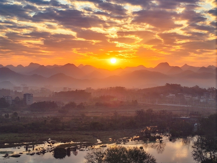 2025年12月15日，广西桂林，太阳从远处的山顶渐渐升起，温暖的阳光照耀着远处的山峦和村庄，映红了湘江，江面上的小舟在收拾渔获，码头广场还有晨练的瑜伽…冬日暖阳晨景美不胜收。来源：唐广东/IC photo