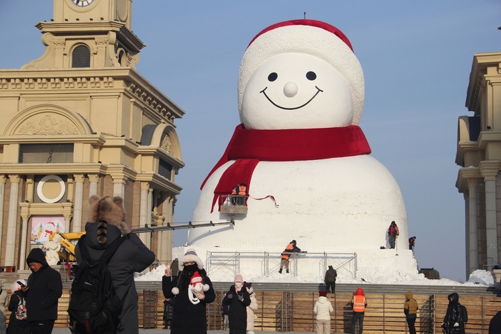 2025年12月15日，黑龙江省哈尔滨市，道里区群力江畔音乐广场上的网红大雪人制作已基本完成，吸引了许多游客前来打卡拍照。 今年的网红大雪人身高19米、长14米、宽11米，比往年高了1米，用雪量增加了1200立方米，总用雪量超3000立方米，达到历年之最。