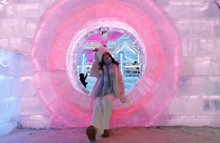 2025年12月20日，黑龙江省哈尔滨市，第二十七届哈尔滨冰雪大世界园区内，梦幻城堡景观区成为冬日焦点。这座最高处达24米的冰建奇观，以13200立方米晶莹剔透的冰堆砌而成，在寒风中闪耀着童话般的光泽。特别设计的圆形打卡点宛如天然画框，吸引众多女游客驻足留影。当人们端坐其间，仿佛置身于冰雪编织的梦境，每一个角落都散发着童话书里才有的浪漫气息，共同构筑起一个晶莹剔透的冰雪乌托邦。