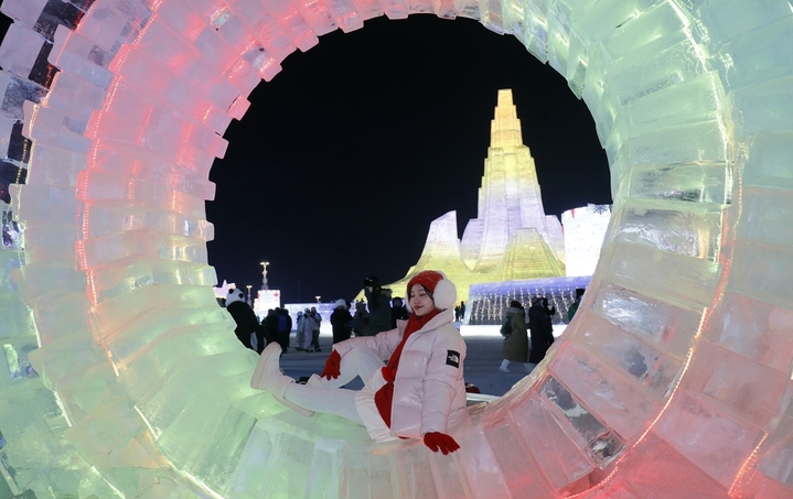 2025年12月20日，黑龙江省哈尔滨市，第二十七届哈尔滨冰雪大世界园区内，梦幻城堡景观区成为冬日焦点。这座最高处达24米的冰建奇观，以13200立方米晶莹剔透的冰堆砌而成，在寒风中闪耀着童话般的光泽。特别设计的圆形打卡点宛如天然画框，吸引众多女游客驻足留影。当人们端坐其间，仿佛置身于冰雪编织的梦境，每一个角落都散发着童话书里才有的浪漫气息，共同构筑起一个晶莹剔透的冰雪乌托邦。