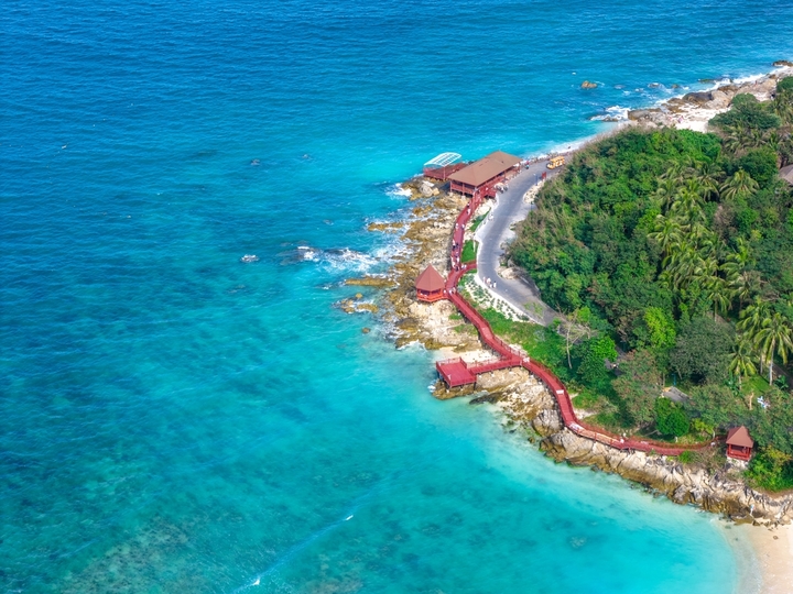 2025年12月15日，海南省三亚市，航拍俯瞰海南三亚蜈支洲岛海浪礁石和环岛公路美丽风光。蜈支洲岛，清澈的海水拍打着礁石形成浪花，电瓶车在环岛公路上穿行，热带海岛风光美醉了。海南旅游风光。大疆御4PRO无人机高清航拍。