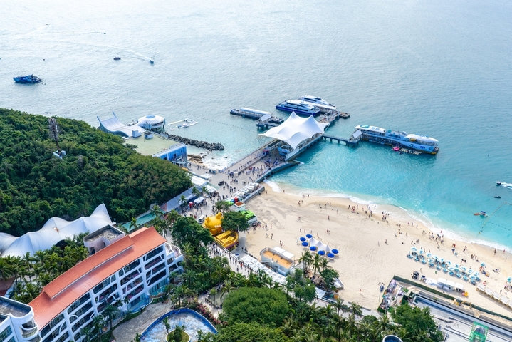 2025年12月15日，海南省三亚市，航拍俯瞰海南三亚蜈支洲岛海浪礁石和环岛公路美丽风光。蜈支洲岛，清澈的海水拍打着礁石形成浪花，电瓶车在环岛公路上穿行，热带海岛风光美醉了。海南旅游风光。大疆御4PRO无人机高清航拍。