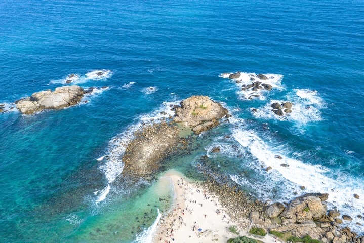 2025年12月15日，海南省三亚市，航拍俯瞰海南三亚蜈支洲岛海浪礁石和环岛公路美丽风光。蜈支洲岛，清澈的海水拍打着礁石形成浪花，电瓶车在环岛公路上穿行，热带海岛风光美醉了。海南旅游风光。大疆御4PRO无人机高清航拍。IC photo