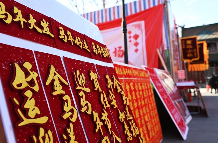 步入市场，红彤彤的挂楣上，“招财进宝”“连年有余”等吉祥话格外醒目；福字、窗花、头花琳琅满目，其中天津非遗绒花尤为抢眼，戴上一朵，瞬间化身“津门富贵花”；手写春联区更是趣味横生，“爱你老已”“有福我就享”等网络热梗春联引人驻足，而“合体字”春联和国潮风窗花则吸引了众多年轻人前来拍照打卡，分享至朋友圈。