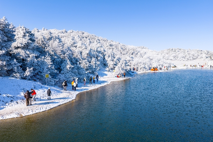 2026年1月21日，杭州临安百丈岭迎来雪后晴天，群山银装素裹，湖水碧蓝如镜，游客沿湖赏雪、拍照、露营，尽享高山雪景与自然静谧之美。