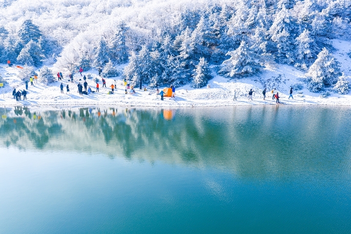 2026年1月21日，杭州临安百丈岭迎来雪后晴天，群山银装素裹，湖水碧蓝如镜，游客沿湖赏雪、拍照、露营，尽享高山雪景与自然静谧之美。