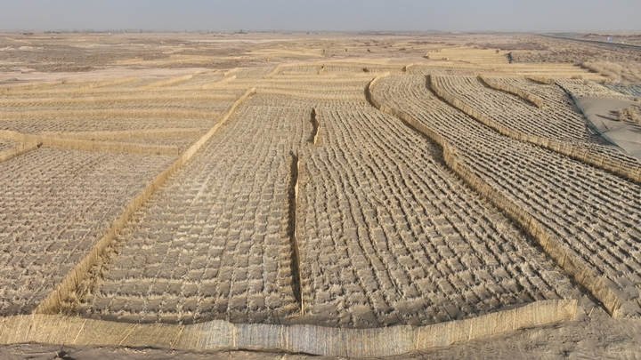 2026年1月22日，在甘肃省酒泉市金塔至大墩门公路两侧连绵起伏的沙丘上，千亩阻沙网与草方格交织成一道道的 “沙海防线”，昔日随风移动的沙丘被牢牢锁住。
