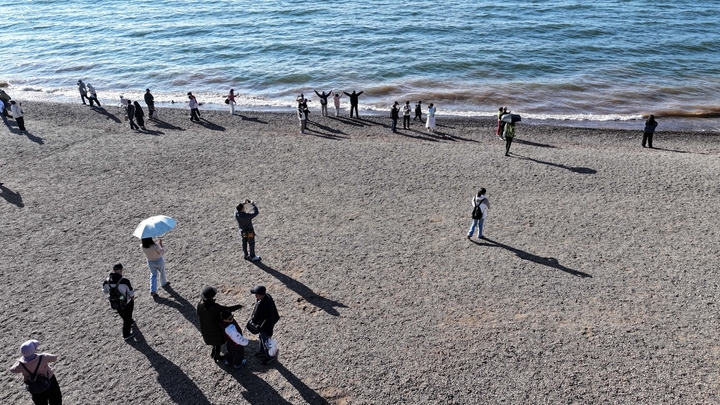 2026年1月29日，在云南省玉溪市抚仙湖沙滩，众多游客在赏景游玩。